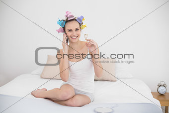 Content natural brown haired woman in hair curlers making a phone call and holding an eyelash curler