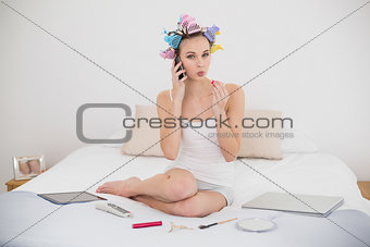 Pouting natural brown haired woman in hair curlers applying gloss while making a phone call