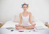 Peaceful natural brown haired woman in hair curlers meditating in lotus position