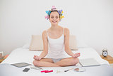 Relaxed natural brown haired woman in hair curlers meditating in lotus position