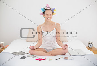 Content natural brown haired woman in hair curlers relaxing in lotus position