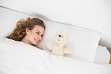 Smiling brunette lying next to teddy bear