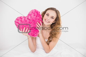 Happy attractive brunette holding heart pillow