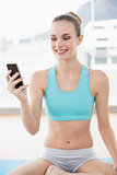 Sporty cheerful woman holding phone while sitting on exercising mat