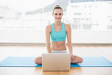 Sporty smiling woman sitting cross-legged in front of laptop