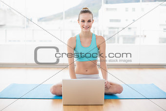 Sporty smiling woman sitting cross-legged in front of laptop