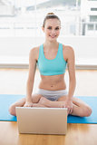 Sporty happy woman sitting cross-legged in front of laptop