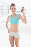 Sporty smiling woman holding up smartphone
