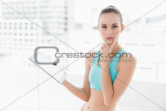 Sporty pensive woman holding a tablet
