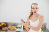 Shocked young woman holding smartphone looking at camera