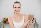 Happy young woman holding smartphone smiling at camera