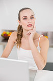 Thoughtful young woman using her laptop looking at camera