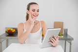 Thinking happy young woman using her tablet at table