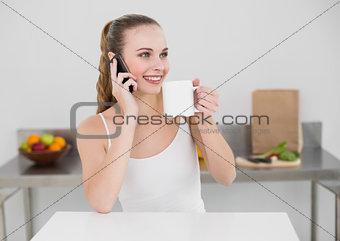 Happy young woman making a phone call and holding a mug