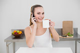 Happy young woman making a phone call and holding a mug looking at camera