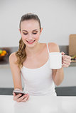 Happy young woman holding a mug and texting with smartphone