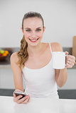 Smiling young woman holding a mug and texting with smartphone