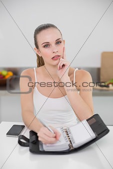 Thoughtful young woman writing in a planner looking at camera