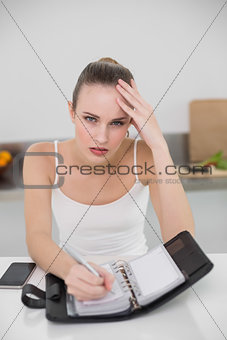 Stressed young woman writing in a planner looking at camera