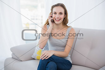 Happy young woman sitting on couch talking on smartphone