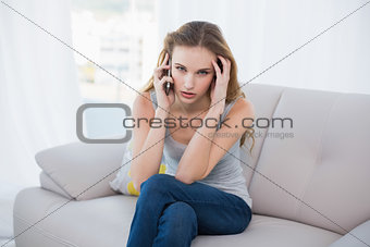 Stressed young woman sitting on couch talking on smartphone