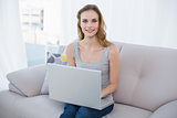 Happy young woman sitting on couch using laptop