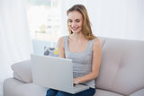 Cheerful young woman sitting on couch using laptop