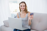Happy young woman sitting on couch using laptop for online shopping