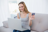 Young woman sitting on couch using laptop for online shopping