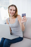 Laughing young woman sitting on couch using laptop for shopping online