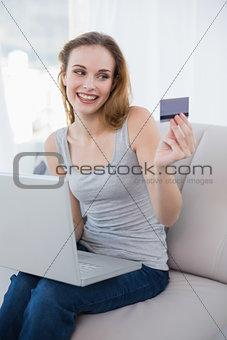 Laughing young woman sitting on couch using laptop for shopping online