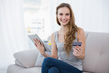 Happy young woman sitting on couch using tablet for shopping online