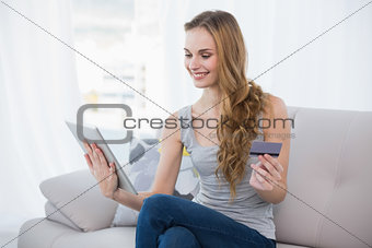 Smiling young woman sitting on couch using tablet for shopping online