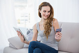 Cheerful young woman sitting on couch using tablet for shopping online