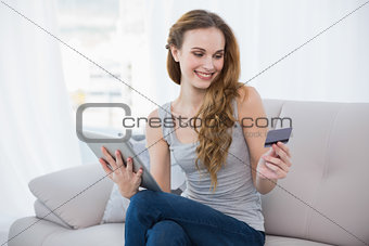Pretty young woman sitting on couch using tablet for shopping online