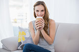 Smiling young woman sitting on couch holding disposable cup
