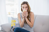 Young woman sitting on couch drinking from disposable cup