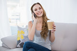 Young woman sitting on couch holding disposable cup on the phone