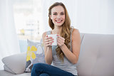 Happy young woman sitting on sofa holding a mug