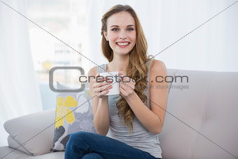 Happy young woman sitting on sofa holding a mug