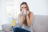 Happy young woman sitting on sofa drinking from a mug