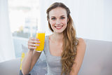Content young woman sitting on sofa holding glass of orange juice