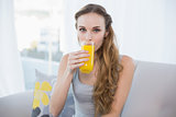 Content young woman sitting on sofa drinking glass of orange juice
