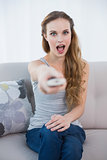 Shocked young woman sitting on sofa watching tv