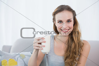 Happy young woman sitting on sofa holding glass of milk