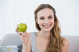 Happy young woman sitting on sofa holding green apple