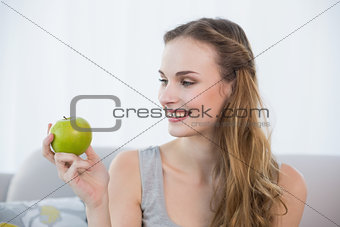 Smiling young woman sitting on sofa holding green apple