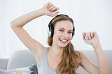 Dancing young woman sitting on sofa listening to music