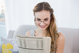 Happy young woman sitting on sofa reading newspaper