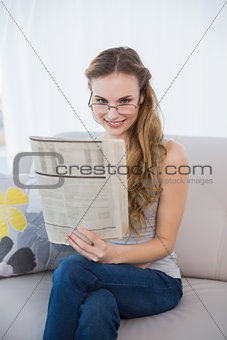 Smiling young woman sitting on sofa reading newspaper